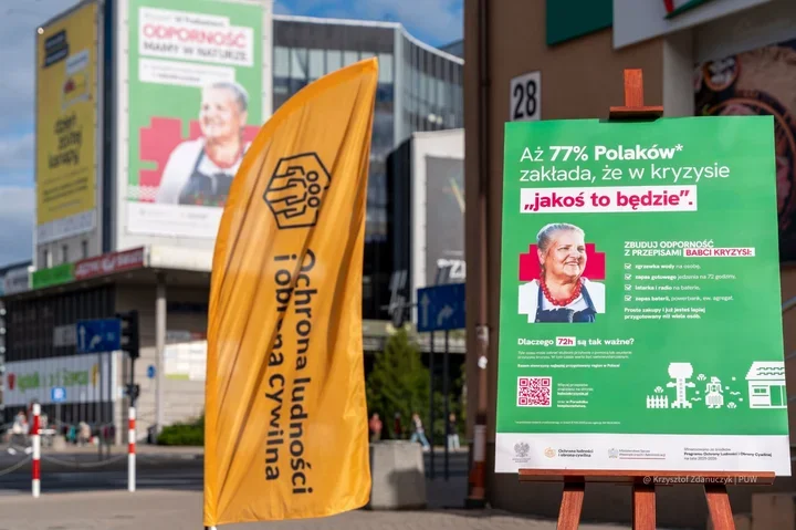 Żółta flaga i plakat informacyjny o odporności w sytuacjach kryzysowych ustawione w przestrzeni miejskiej.