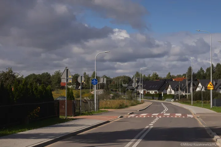 Nowo wybudowana droga z przejściem dla pieszych, chodnikami i znakami drogowymi na osiedlu domków jednorodzinnych podczas dnia.