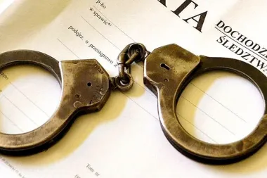 Metalowe kajdanki leżą na polskim dokumencie śledczym z nagłówkiem dotyczącym dochodzenia.