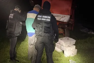 Funkcjonariusze Straży Granicznej zatrzymują mężczyznę przy przyczepie z ładunkiem, obok leżą pakunki owinięte folią.