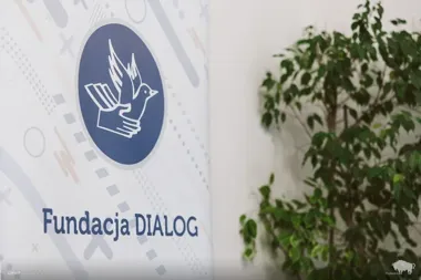 Fragment baneru Fundacji DIALOG z logo przedstawiającym gołębia i dłonie, obok rośliny doniczkowej.