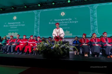 Uroczysta inauguracja roku akademickiego 2026/2027 na scenie z uczestnikami w togach i biretach, w tle ekran z napisem „Inauguracja Roku Akademickiego 2026/2027