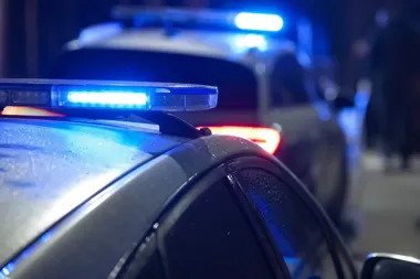 Dwa policyjne radiowozy z włączonymi niebieskimi światłami nocą na ulicy.