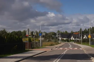 Nowo wybudowana droga z przejściem dla pieszych, chodnikami i znakami drogowymi na osiedlu domków jednorodzinnych podczas dnia.