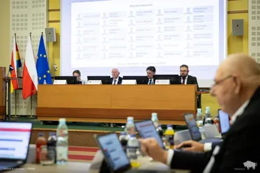 Posiedzenie w auli z udziałem osób przy stole prezydialnym i uczestnikami z tabletami, na ekranie wyświetlone wyniki kworum.
