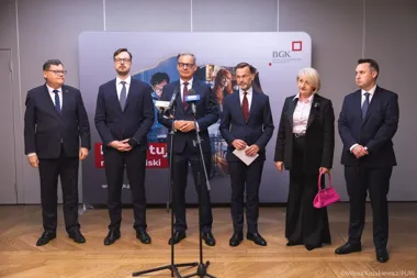 Sześć osób w formalnym stroju stoi podczas konferencji prasowej przed ścianką z logo BGK.